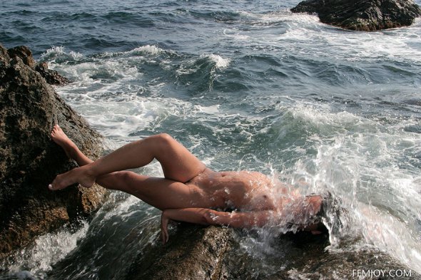 Брюнетка позирует на камнях у моря